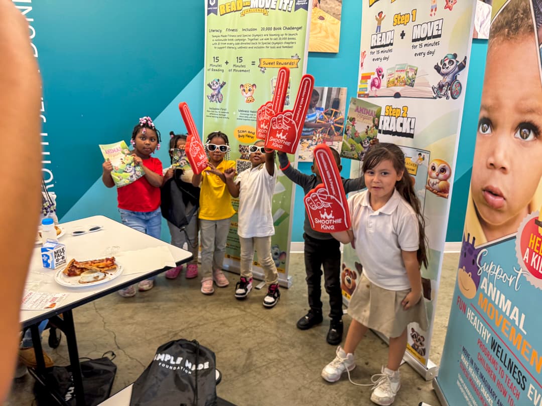 Children holding Animal Movements workbooks and celebration items beside Read and Move It banners